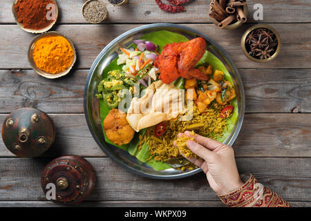 Overhead view of Indian woman's hand eating biryani rice on wooden dining table. Stock Photo