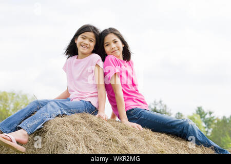 two young girls sitting on top of haybale Stock Photo