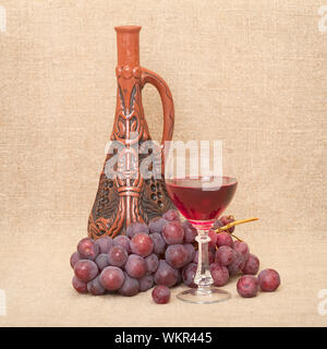 Still-life with a clay bottle, grapes and a glass on a canvas background Stock Photo