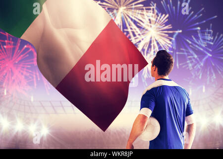 Handsome italian football player in blue jersey against fireworks exploding over football stadium Stock Photo