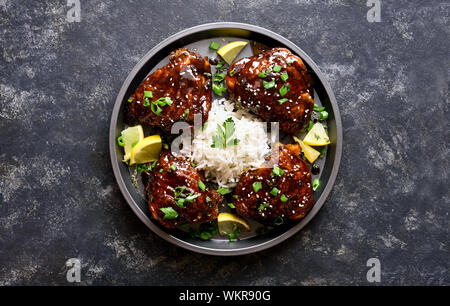 Baked chicken thighs with rice over dark stone table. Grilled chicken thighs in honey soy sauce. Tasty food in asian style. Top view, flat lay Stock Photo