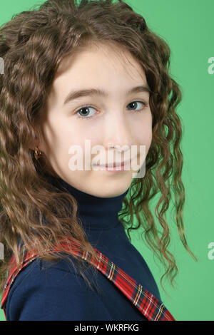 Portrait of adorable smiling schoolgirl with curl hair standing isolated on a green background. High resolution photo. Full depth of field. Stock Photo