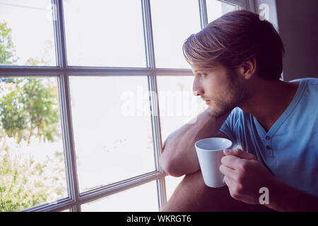 Thoughtful man sitting by the window having coffee at home in the living room Stock Photo