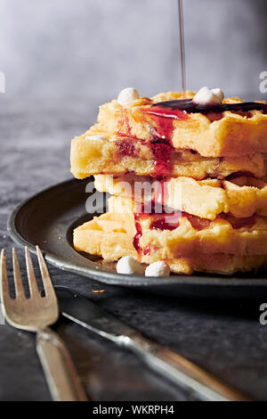 Tasty appetizing waffle with red syrup on plate on black concrete background. Frontal view. Vertical. With copy space for text. Stock Photo