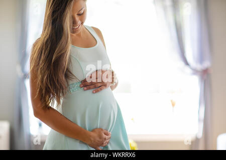 Smiling pregnant woman in dress with her hands at belly Stock Photo