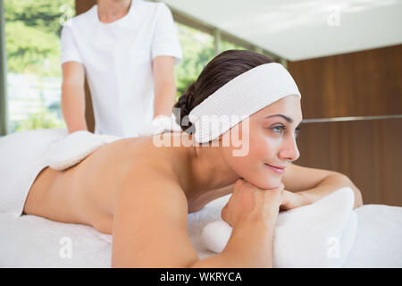 Beauty therapist rubbing smiling womans back with heated mitts in the health spa Stock Photo