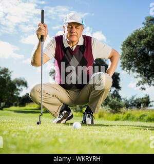 Golfer kneeling watching gold ball on a sunny day at the golf course Stock Photo