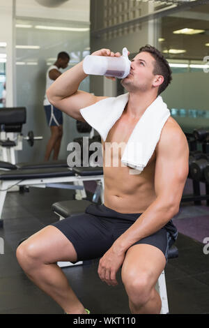 Shirtless young man drinking protein shake in gym Photograph by