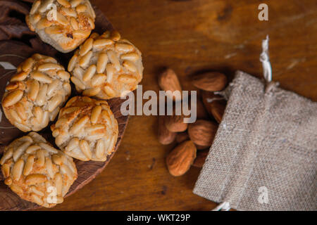 Closeup plate with Catalan panellets and some roasted almonds in a small bag on a wooden table. Typical desert in Catalonia for La Castanyada Stock Photo