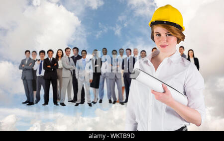 Pretty young architect smiling at camera against blue sky with white clouds and business people Stock Photo