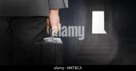 Businessman holding briefcase against grey staircase leading to open door Stock Photo