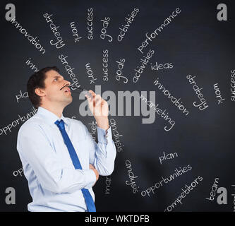 Thinking businessman biting glasses against blackboard with business buzzwords Stock Photo