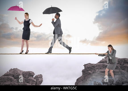 Young businesswoman pulling a tightrope for business people against rocky landscape Stock Photo