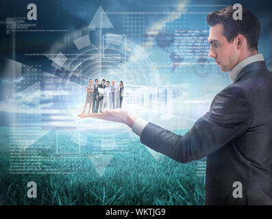 Business team looking at camera held by giant businessman against blue sky over green field Stock Photo