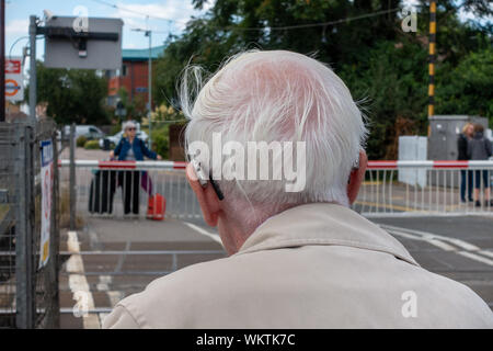 Closeup rear view of an grey haired elderly man waiting at train crossing Stock Photo