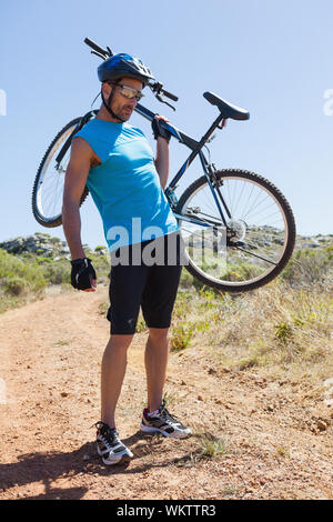 Fit cyclist carrying his bike out in the countryside on a sunny day Stock Photo