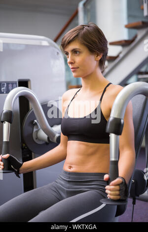 Focused brunette using weights machine for arms at the gym Stock Photo