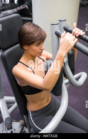 Focused brunette using weights machine for arms at the gym Stock Photo