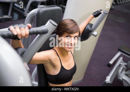 Focused brunette using weights machine for arms at the gym Stock Photo