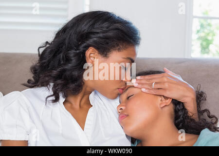 Concerned mother cuddling sick daughter at home in living room Stock Photo