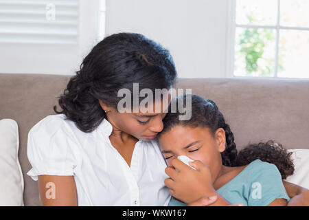 Concerned mother cuddling sick daughter at home in living room Stock Photo