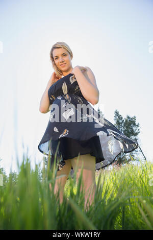 Pretty blonde in sundress smiling at camera on a sunny day in the countryside Stock Photo