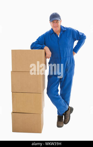 Happy delivery man leaning on pile of cardboard boxes on white background Stock Photo