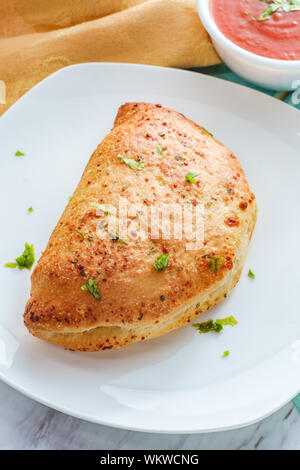 Italian pastry pepperoni and cheese calzone with tomato marinara dipping sauce Stock Photo