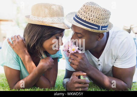 Happy couple lying in garden together smelling flowers on a sunny day Stock Photo