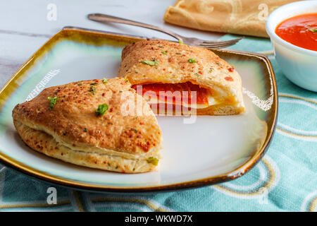Italian pastry pepperoni and cheese calzone with tomato marinara dipping sauce Stock Photo