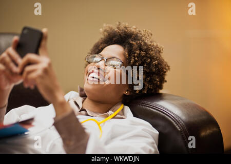 Female doctor taking a break, and text messaging on a sofa. Stock Photo