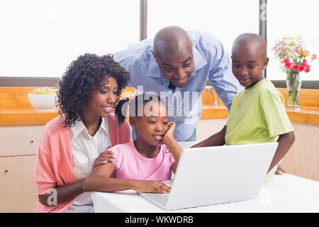 Cute siblings using laptop together with parents at home in the kitchen Stock Photo