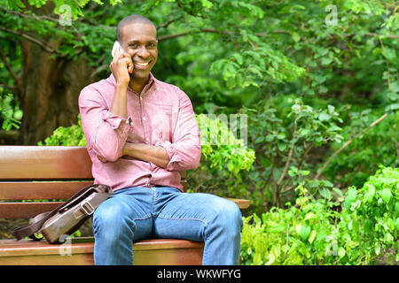 Casual man sitting on park bench and talking on cell phone Stock Photo