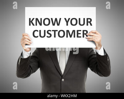A business man holding a paper in front of his face with the text know your customer Stock Photo