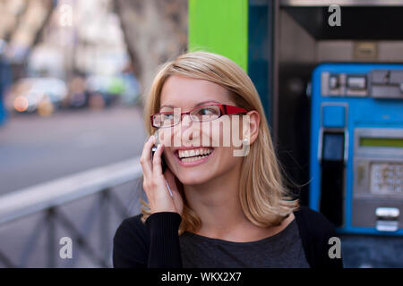 Young relaxed woman talking on the cell phone with the retro phone boot in the background. Stock Photo