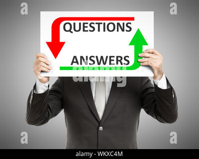 A business man holding a paper in front of his face with the text questions answers Stock Photo