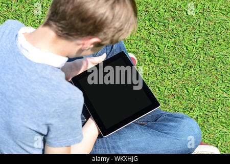 Boy sitting on lawn and using his new tablet pc Stock Photo