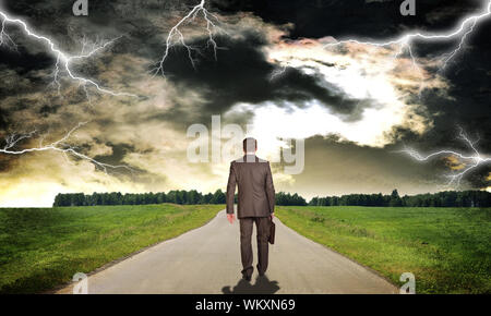Businessman in suit with briefcase walking on the road ahead. Rear view Stock Photo