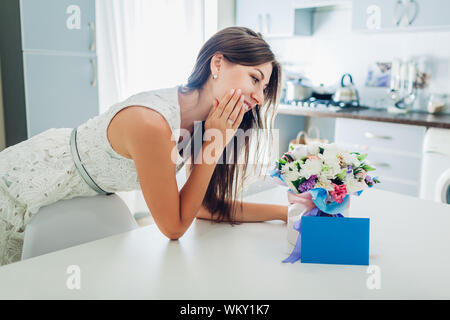 Woman found bouquet of flowers in gift box and envelope with card on kitchen. Surprise. Present for holiday Stock Photo