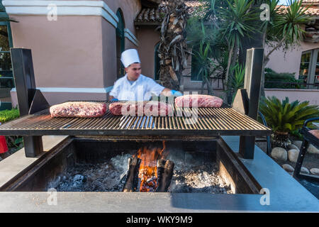 Chef preparing many large cuts of meat of prime rib on outdoor grill by smoking it for two hours and then cooking it in the oven for another two hours Stock Photo