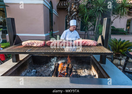 Chef preparing many large cuts of meat of prime rib on outdoor grill by smoking it for two hours and then cooking it in the oven for another two hours Stock Photo