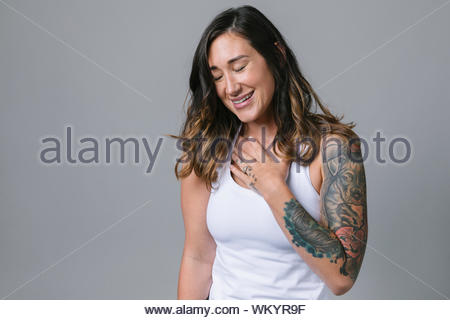 Portrait happy young woman with tattoos and hand over heart