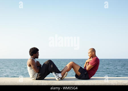 young african american man and hispanic friend doing series of sit-ups along the Caribbean sea in Havana, Cuba. Horizontal shape, full length, side vi Stock Photo