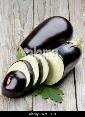Ripe Raw Eggplants Full Body and Slices with Leafs isolated on Rustic Wooden background Stock Photo