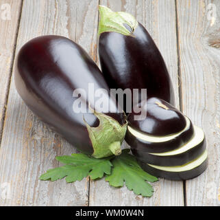 Stack of Ripe Raw Eggplants Full Body and Slices with Leafs isolated on Rustic Wooden background Stock Photo