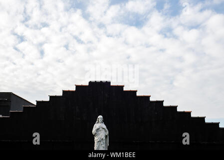 Jesus monument over a grave in the Calvary Cemetery of Woodside Queens, New York. Roofline in the background is for a building outside of the cemetery Stock Photo