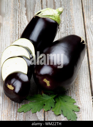 Full Body and Slices of Ripe Raw Eggplants with Leafs isolated on Rustic Wooden background Stock Photo
