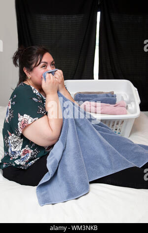Latina woman on her bed folding towels and holding one close to her face Stock Photo