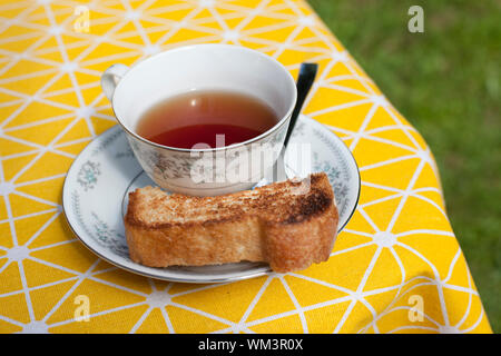 Snack and drink outside with teacup, spoon, saucer and toast on a yellow tablecloth Stock Photo