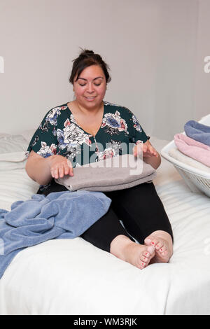 Woman folding fluffy towels on the bed at home smiles down into her work Stock Photo
